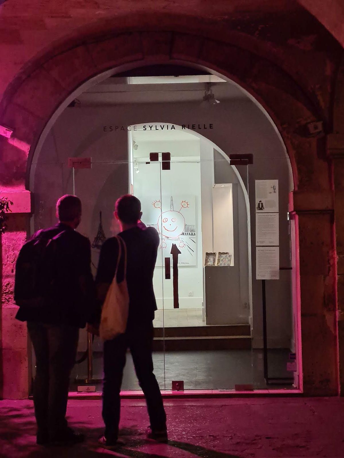 Silhouettes at the entrance to Galerie Sylvia Rielle under a pink-lit archway