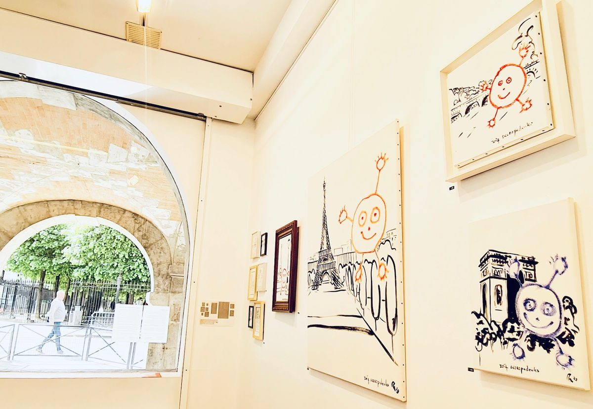 Gallery interior with drawings on the wall and a view through an arch to Place des Vosges park