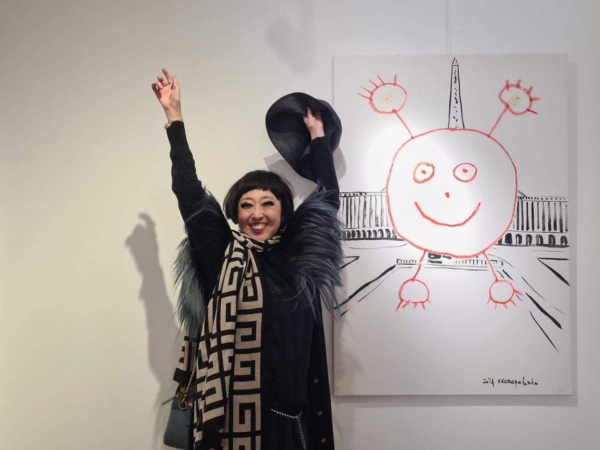 Zoia Skoropadenko in a black beret beside a large white canvas with a red smiling sun drawing